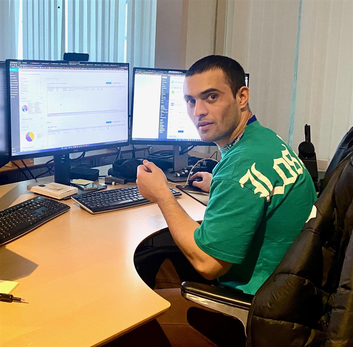 En grønnkledd mann sitter foran to dataskjermer som står på et bord. Fotografi. - Klikk for stort bilde